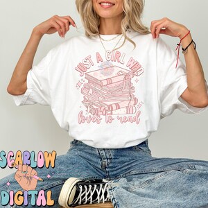 Puede incluir: Camiseta blanca con un gr&aacute;fico rosa que dice "Just a girl who loves to read" y presenta una pila de libros con un dise&ntilde;o floral.
