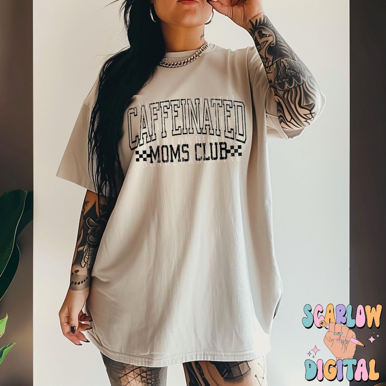 K&ouml;nnte beinhalten: Ein hellgraues Oversize-T-Shirt mit schwarzem Text, der "CAFFEINATED MOMS CLUB" in einer Schriftart im College-Stil lautet.