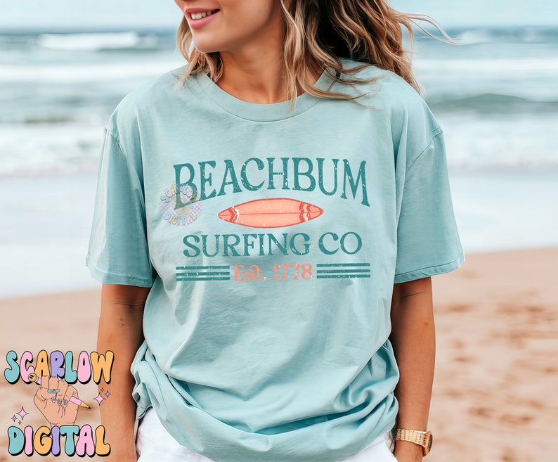 May include: A light blue t-shirt with a graphic design that says "Beachbum Surfing Co. Est. 1778" with a surfboard and a floral design.