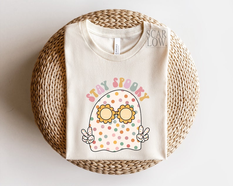 May include: A white t-shirt with a cartoon ghost wearing sunglasses and the text "Stay Spooky" in a retro font.