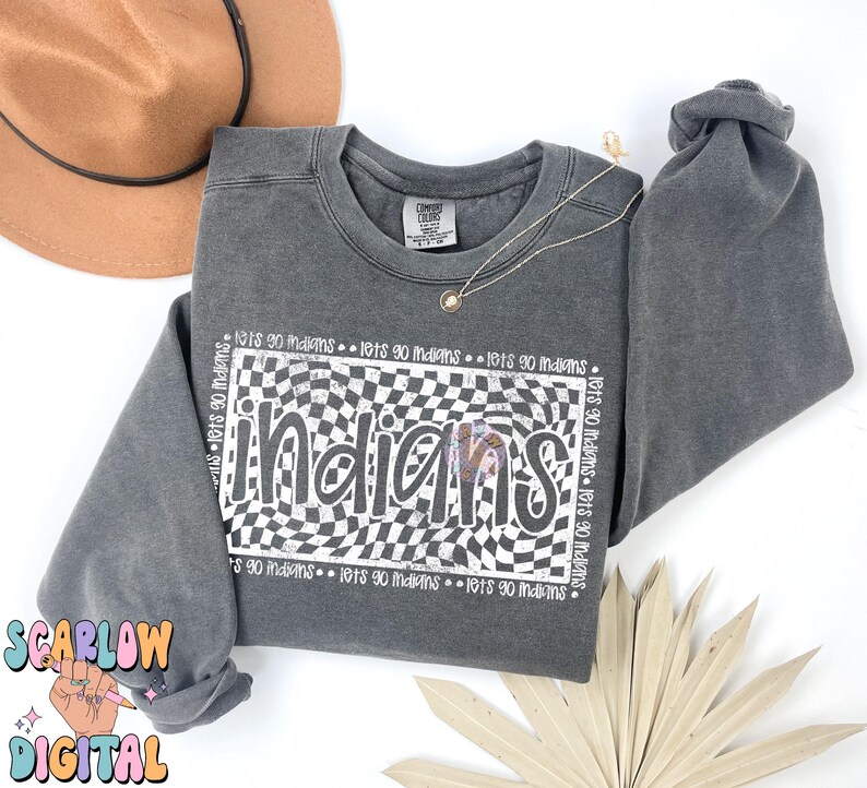 May include: A grey sweatshirt featuring the word "Indians" in a white and black checkered pattern. The phrase "lets go indians" is repeated around the design. A brown hat and gold necklace are also visible.