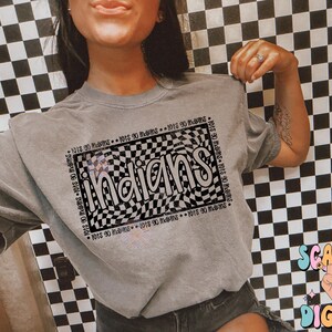 May include: A grey t-shirt featuring the word "Indians" in a black and white checkered pattern. The text is surrounded by the words "1015 90 mams". The shirt has a relaxed fit.