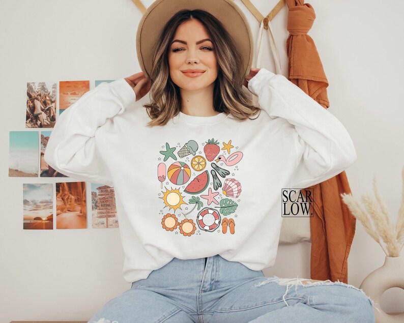 K&ouml;nnte beinhalten: Wei&szlig;er Pullover mit einem bunten, sommerlichen Grafikdruck, der eine Wassermelone, einen Strandball, einen Seestern, ein Eis am Stiel und andere sommerliche Symbole zeigt. Der Text "SCAR LOW." ist in der unteren rechten Ecke des Bildes sichtbar.
