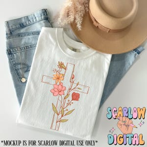 May include: White t-shirt with a floral cross design. The cross is outlined in brown and the flowers are pink, yellow, and orange. The text "Scarlow Digital" is in the lower right corner of the image.