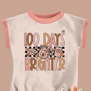 May include: A pink and white t-shirt with a graphic design that says "100 Days Brighter" with a school bus, backpack, and books.