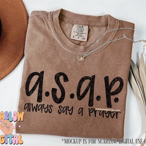 May include: A brown t-shirt with the text "a.s.a.p. always say a prayer" printed on it in black.