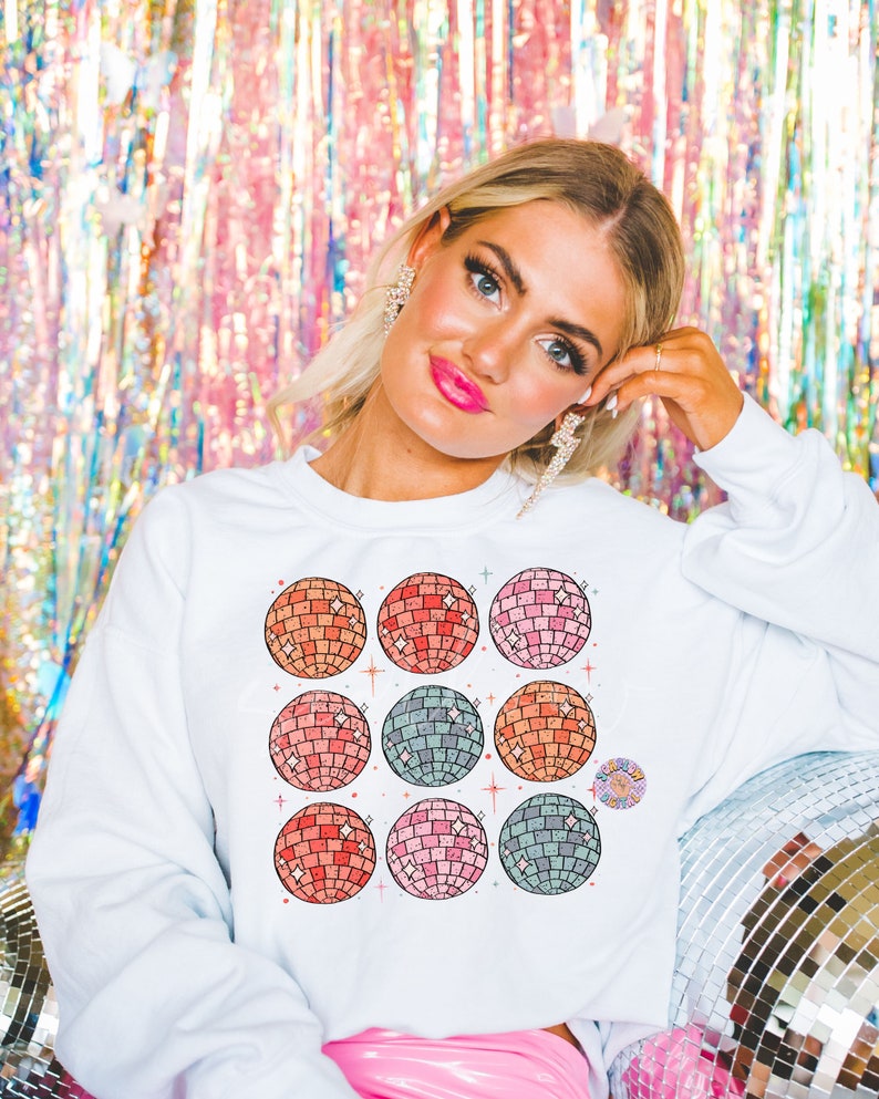 May include: White sweatshirt with a colorful design of nine disco balls. The disco balls are arranged in a 3x3 grid and have a retro, vintage aesthetic.