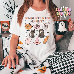 Puede incluir: Camiseta blanca con un estampado gr&aacute;fico de art&iacute;culos de tem&aacute;tica de Halloween y el texto "Things that make me happy". El gr&aacute;fico incluye calabazas, murci&eacute;lagos, calaveras, gatos negros, fantasmas, brujas, cementerios y caramelos.