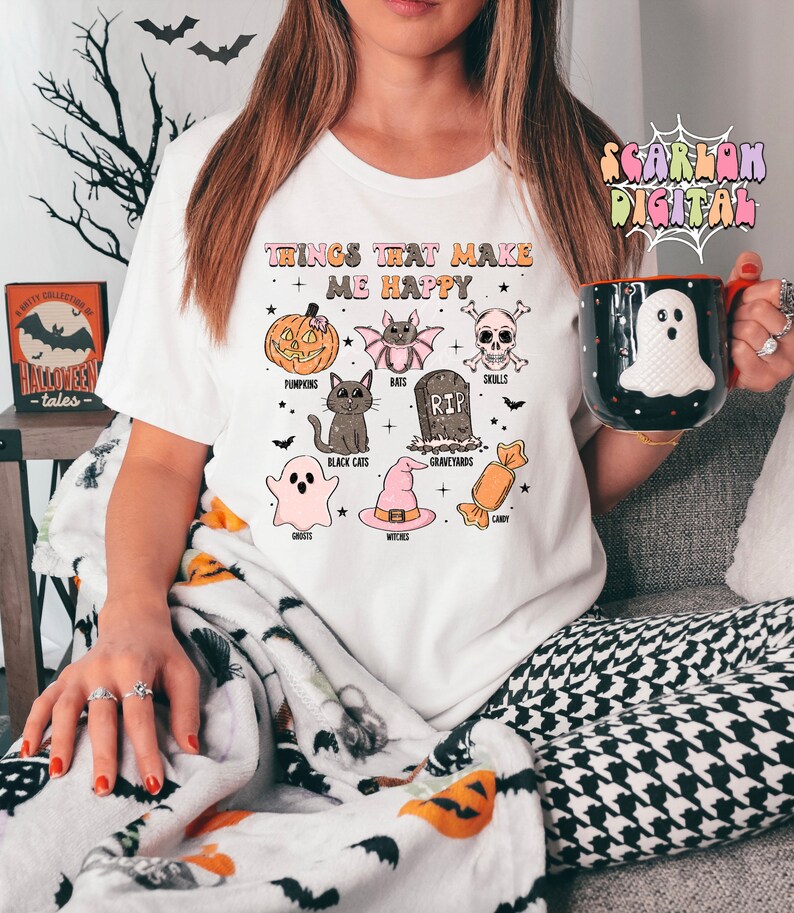 Puede incluir: Camiseta blanca con un estampado gr&aacute;fico de art&iacute;culos de tem&aacute;tica de Halloween y el texto "Things that make me happy". El gr&aacute;fico incluye calabazas, murci&eacute;lagos, calaveras, gatos negros, fantasmas, brujas, cementerios y caramelos.