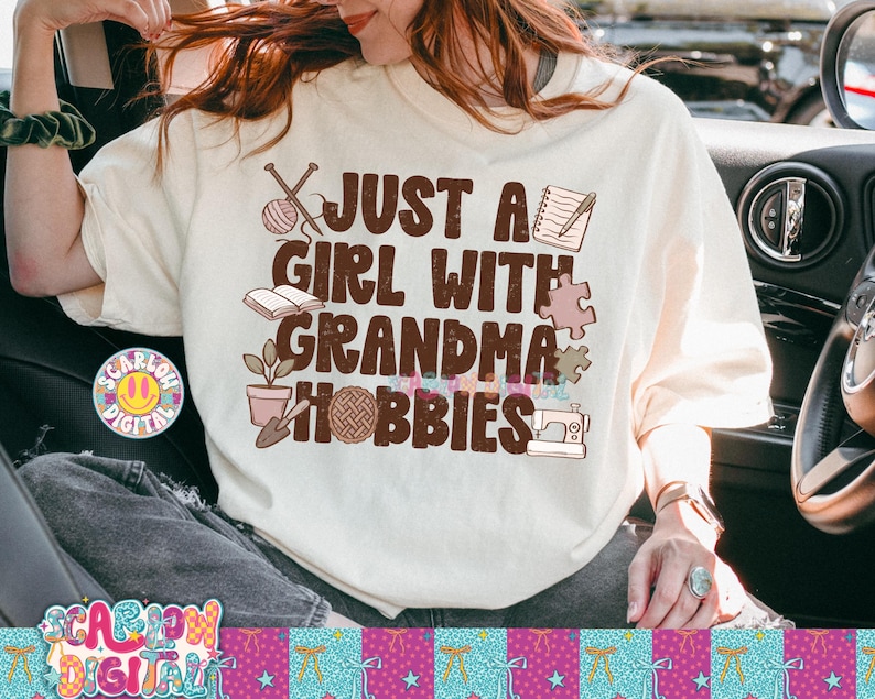 K&ouml;nnte beinhalten: Cremefarbenes T-Shirt mit dem Text "JUST A GIRL WITH GRANDMA HOBBIES" in Braun. Das Shirt zeigt Illustrationen von Stricknadeln, einem Wollkn&auml;uel, einem Buch, einem Notizblock, einem Puzzleteil, einer Topfpflanze, einem Wollkn&auml;uel und einer N&auml;hmaschine.