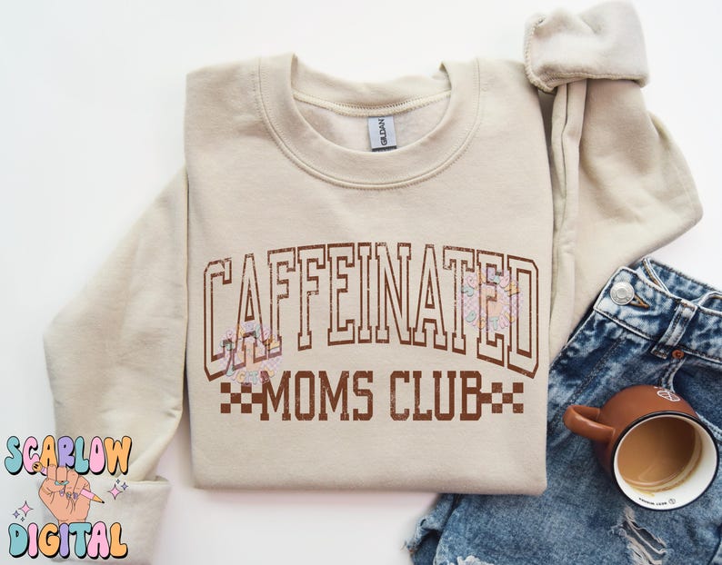 K&ouml;nnte beinhalten: Ein beiger Pullover mit dem Text "CAFFEINATED MOMS CLUB" in braunen Buchstaben mit einem karierten Design darunter. Der Pullover hat einen Rundhalsausschnitt und lange &Auml;rmel.
