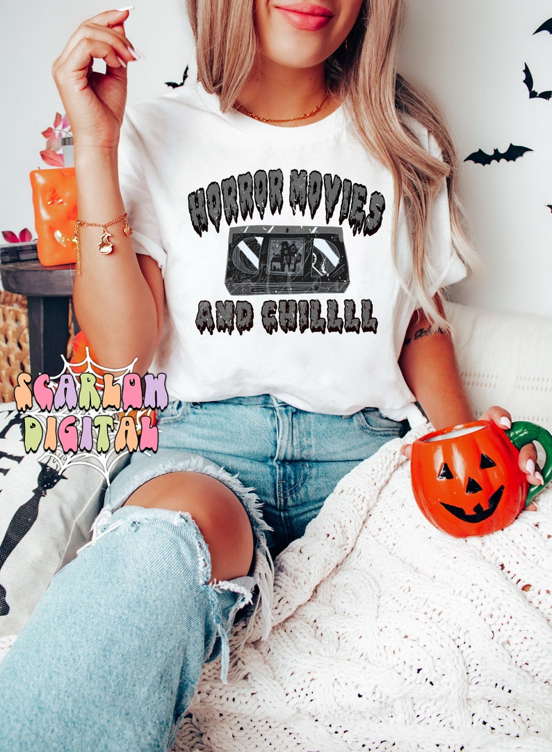 May include: A white t-shirt with the text "Horror Movies and Chilll" in black dripping letters. A black and white image of a VHS tape is in the center of the text.