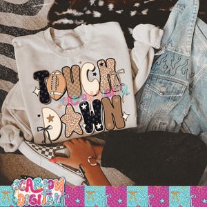 May include: A cream-colored sweatshirt with the words "TOUCH DOWN" in a mix of fonts and patterns, including a football graphic and star accents. A denim jacket and checkered sneakers are also visible.