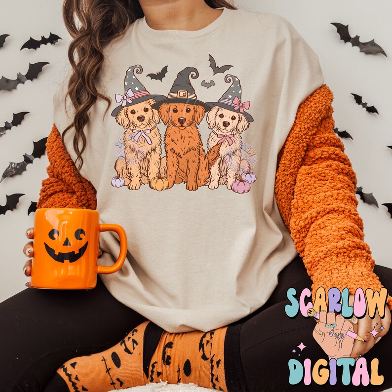 K&ouml;nnte beinhalten: Ein beiger Pullover mit einem Aufdruck von drei Golden Retrievern, die Hexenh&uuml;te tragen. Die Hunde sitzen in einer Reihe und haben ein verspieltes Halloween-Thema.