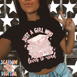 Puede incluir: Una camiseta negra con el texto "Just a girl who loves to read" en letras rosas. Detr&aacute;s del texto se ilustra una pila de libros rosas con p&aacute;ginas blancas.