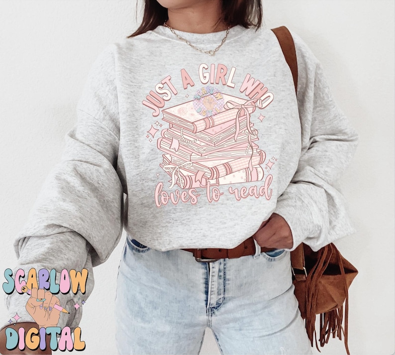 Puede incluir: Una sudadera gris con el texto "Just a girl who loves to read" en letras rosas. El texto est&aacute; rodeado de una pila de libros con flores rosas en el libro de arriba.