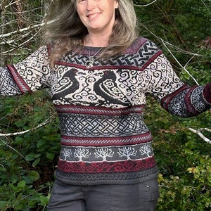 May include: A woman wearing a black and red patterned sweater with a geometric design, black pants, and black shoes. She is standing in a forest with trees behind her.