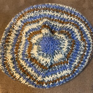 May include: A blue, brown, and white knitted beret with a circular design.