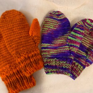 May include: Two pairs of knitted mittens. One pair is orange and the other pair is a mix of purple, green, and pink.