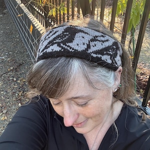 Puede incluir: Una diadema de punto negra y gris con un patrón geométrico. La diadema la lleva puesta una persona con el pelo gris.