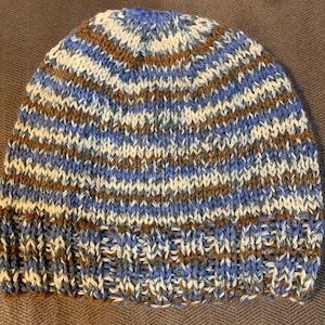 Può includere: Un cappello lavorato a maglia con un motivo a righe in tonalità di marrone, blu e bianco.