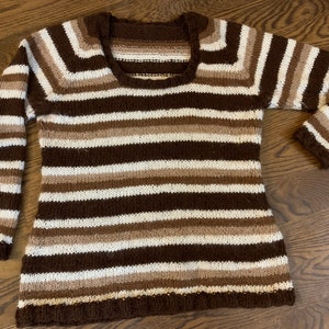 May include: A brown, white, and beige striped knitted sweater with a scoop neck.