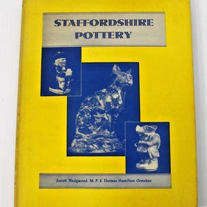 May include: A yellow book cover titled Staffordshire Pottery with the text Josiah Wedgwood, M. P. & Thomas Hamilton Ormsbee. The cover features three blue rectangular insets displaying monochrome photographs of ceramic figurines including a cat.