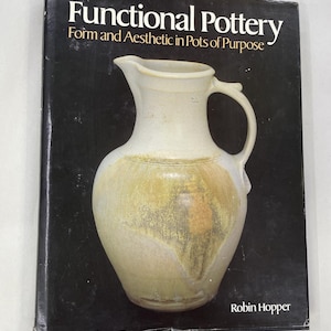 May include: A hardcover book titled Functional Pottery: Form and Aesthetic in Pots of Purpose by Robin Hopper. The black cover features a large, centered image of a cream-colored ceramic pitcher with a textured, mottled yellow-brown glaze.