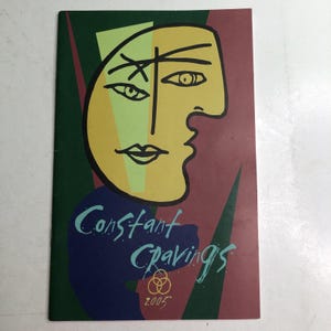 May include: A rectangular booklet cover featuring a stylized yellow face with black line art, set against a background of dark green, maroon, and light green geometric shapes. The text Constant Cravings is printed in blue, with the year 2005 below.