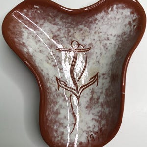 May include: A three-lobed ceramic dish with a glossy finish, featuring a speckled white and brown interior and a solid brown rim. The center displays a brown line-art anchor graphic, and the bottom right corner includes the hand-painted text 1975.