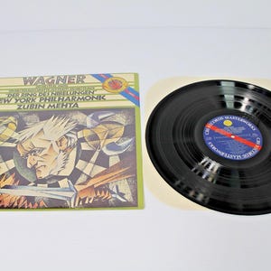 May include: A vinyl record and its square cardboard sleeve featuring an illustration of a man with white hair. The text reads WAGNER, DER RING DES NIBELUNGEN, NEW YORK PHILHARMONIC, ZUBIN MEHTA, and CBS RECORDS-MASTERWORKS on the blue center label.