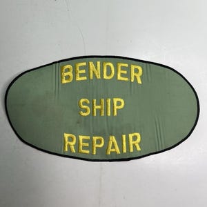 May include: An oval-shaped patch with a sage green fabric background and a black stitched border. The text BENDER SHIP REPAIR is embroidered in yellow capital letters across the center of the patch in three stacked lines.