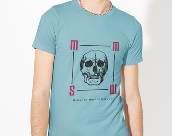 May include: A light blue t-shirt with a black and white skull graphic inside a square with the letters "M S M W" and the text "Memento Mori Streetwear" below the graphic.