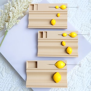 Può includere: Tre mensole espositive in legno color beige chiaro, ciascuna con un limone e oggetti gialli a forma di limone. I limoni sono di un giallo brillante. Le mensole hanno un design unico con un piccolo ritaglio rettangolare.