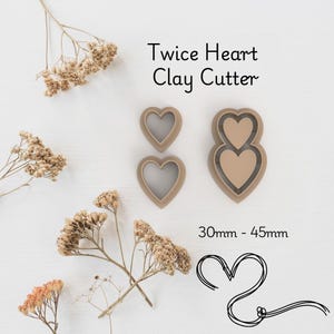 May include: A set of tan-coloured Twice Heart Clay Cutters. The set includes two single heart cutters and one double heart cutter. The text "Twice Heart Clay Cutter" is displayed above the cutters. The size range is 30mm - 45mm.