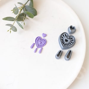 May include: A set of purple and grey heart-shaped cookie cutters. The cutters have intricate designs and are perfect for making decorative cookies.