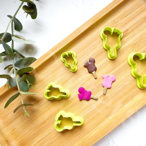 May include: A set of green plastic cookie cutters shaped like ice cream cones and popsicles on a wooden surface.