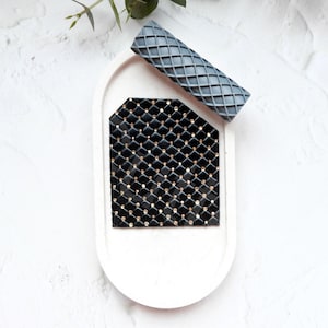 May include: A white ceramic tray with a black and gold geometric design. The tray is on a white background.