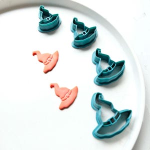 May include: A set of six witch hat cookie cutters, five are teal blue and one is orange. The cutters are on a white plate.