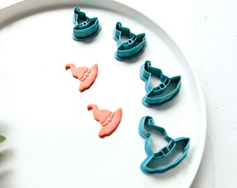 Op de afbeelding: Een set van zes heksenhoed koekjesuitstekers, vijf zijn teal blauw en één is oranje. De uitstekers liggen op een wit bord.