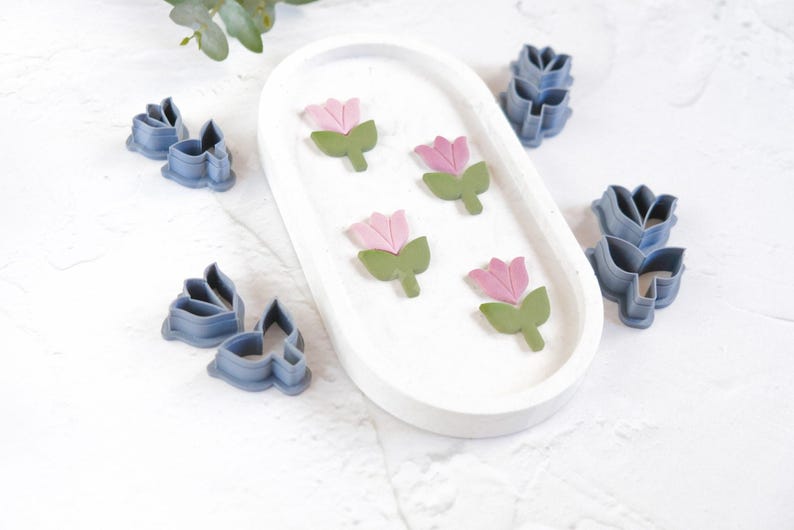 May include: A set of pink and green flower cookie cutters and blue flower cookie cutters on a white surface.