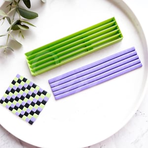 Puede incluir: Un plato blanco con tres herramientas para hacer arcilla polimérica. Las herramientas son un rectángulo de plástico verde con ranuras, un rectángulo de plástico morado con ranuras y un cuadrado a cuadros negro y verde.