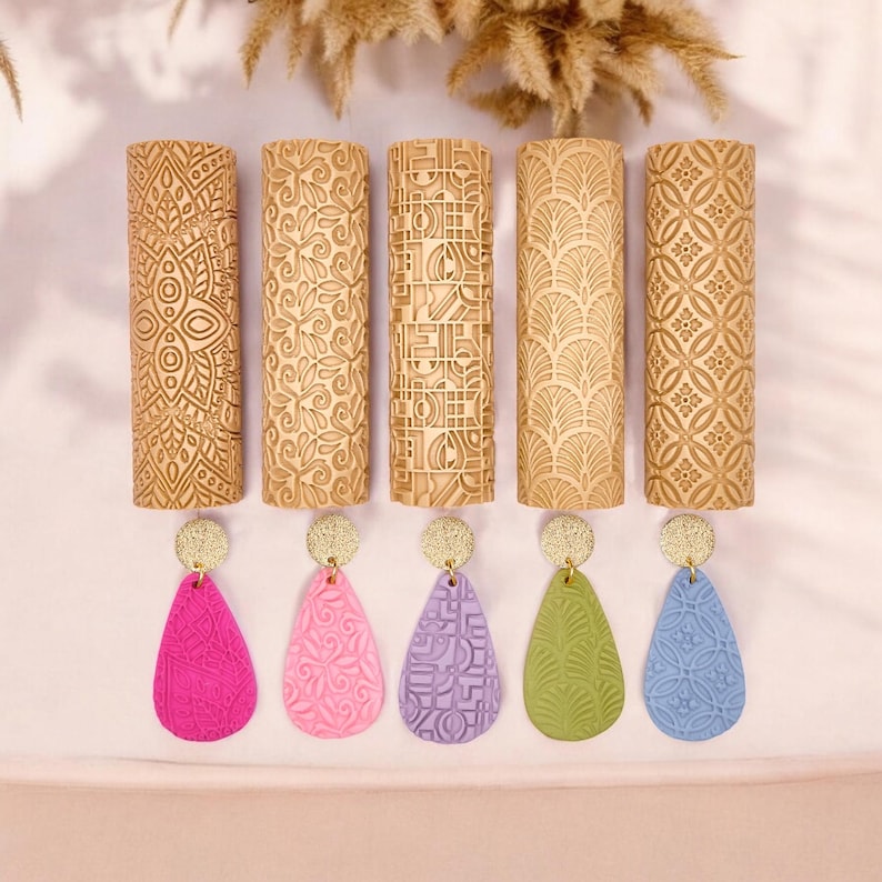May include: Five wooden rolling pins with various embossed patterns, displayed above five colorful teardrop earrings. The earrings are in shades of pink, purple, green, and blue, each with a unique textured design and gold accents.