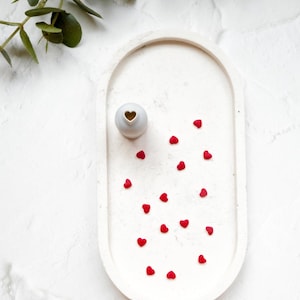 May include: White oval tray with a small white vase with a heart cutout and red heart sprinkles inside.