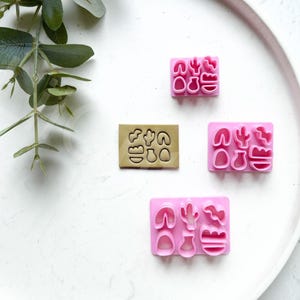 Puede incluir: Cuatro moldes de plástico rosa y uno marrón para hacer decoraciones de fondant o arcilla polimérica. Los moldes presentan varias formas de cactus y plantas.