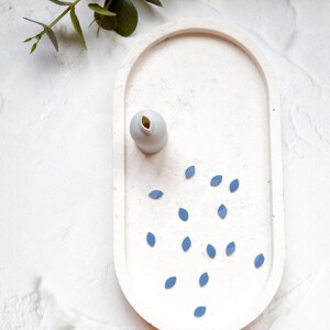 Peut inclure: Un plateau ovale blanc avec un petit vase blanc et des accents en forme de feuille bleue éparpillés sur la surface.