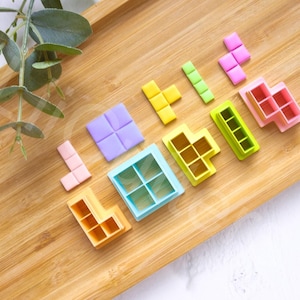 May include: A set of colorful plastic Tetris-shaped cookie cutters on a wooden surface. The cutters are arranged to spell out the word "LOVE".