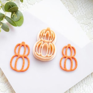 May include: Three orange pumpkin-shaped cookie cutters. One is a complete cutter, and two are individual cutouts. The cutters are made of plastic and are designed for making pumpkin-shaped cookies or other treats.