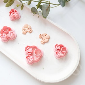 Op de afbeelding: Een set van vijf roze plastic koekjesvormen in de vorm van een konijn. De vormen zijn gerangschikt op een wit bord.