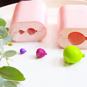 Puede incluir: Dos moldes de silicona rosa para hacer objetos con forma de globo. Hay tres pequeños objetos con forma de globo en diferentes colores: morado, rosa y verde.